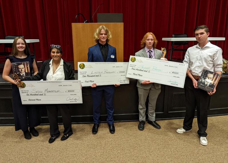 Five debate team winners hold checks and prizes