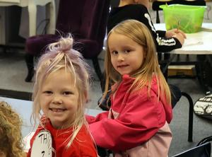 Two girls dressed in red work at a desk and turn to face the camera.
