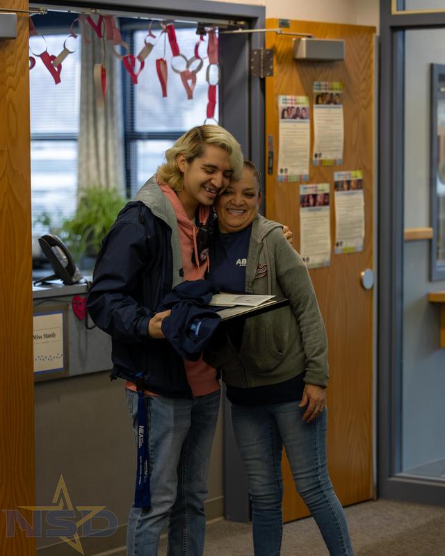 Shane Munoz hugs his mom Maria Munoz while holding his certificate and gifts.