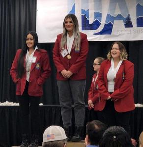 Jesamyn Miller, in a red blazer, stands on the winner\'s podium with the 2nd and 3rd place winners.