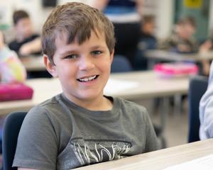 Young boy in gray T-shirt smiles at the camera.