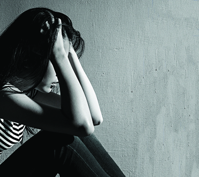 Teen girl sits on floor with elbows on knees and head in hands.
