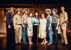 The director poses onstage with cast wearing western clothing at Nampa High.