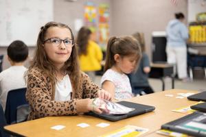 Girl in leopard print sweater and tortoise shell glasses smiles at her desk.