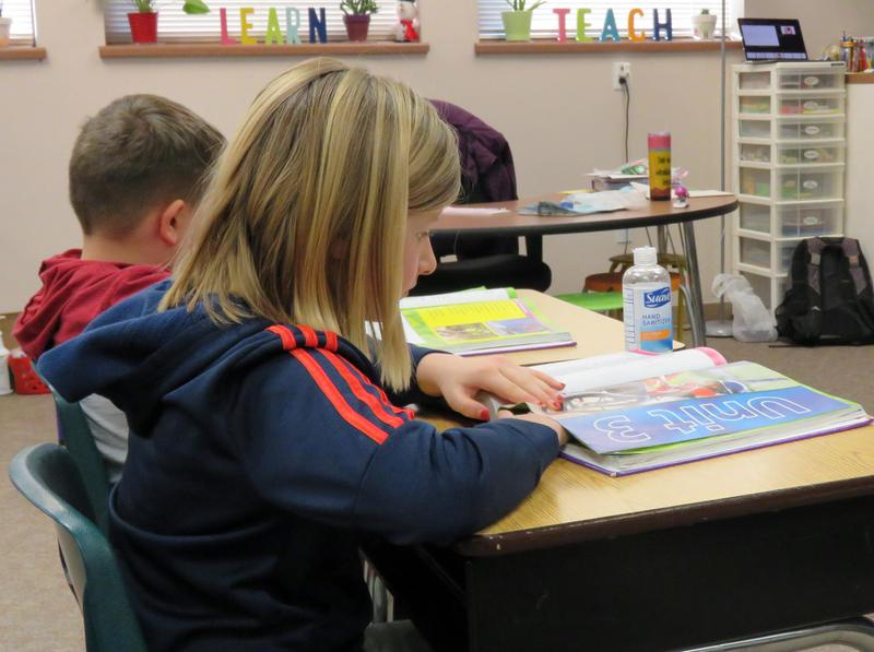A fifth-grader flips through an ELA textbook on her desk.