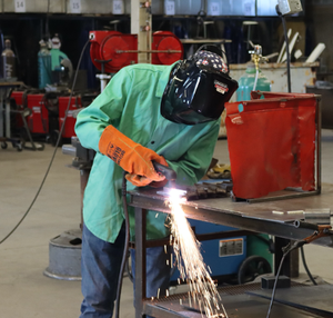 Student in green smock and safety gear welds