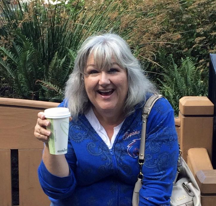 Tina holds a cup of coffee and smiles at the camera.
