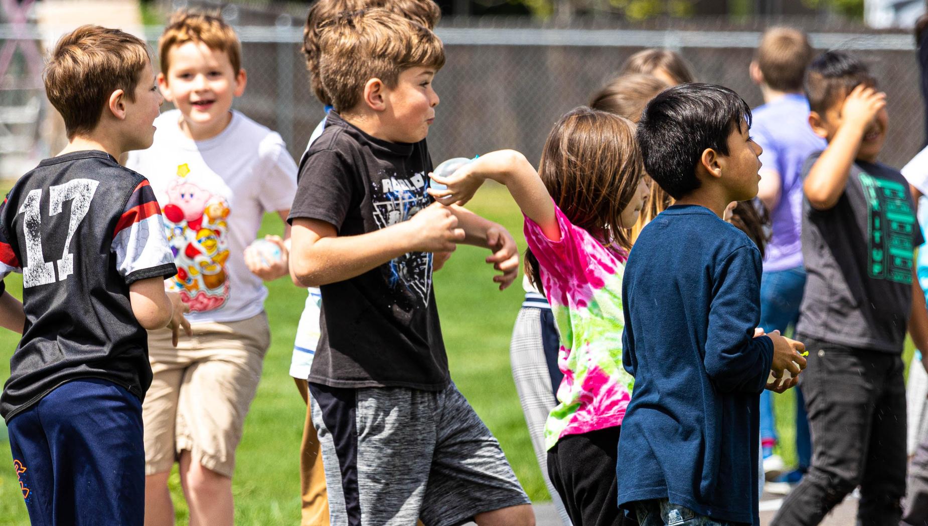 Boy in black shirt reacts to girl preparing to throw a water balloon.