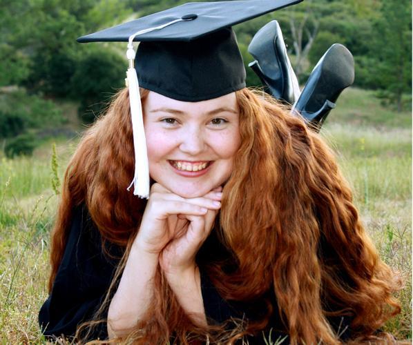 Female graduate lying in field with chin in hands.
