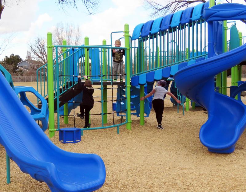 Two young boys and a teen girl play on blue and green school playground equipment.