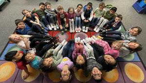 Overhead view of kids sitting on the floor in a circle, showing off their shoes.
