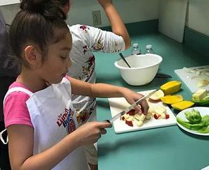 Young girl dressed in pink top and an apron chops apples.