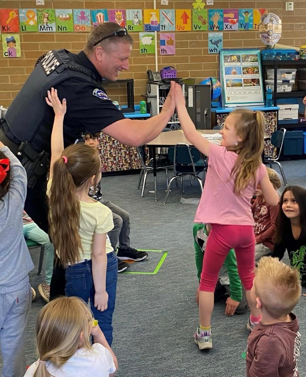 Officer high-fives a young student in the classroom.