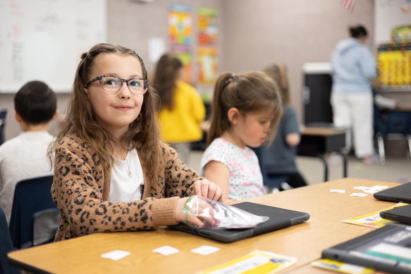 Girl in leopard print sweater and tortoise shell glasses smiles at her desk.