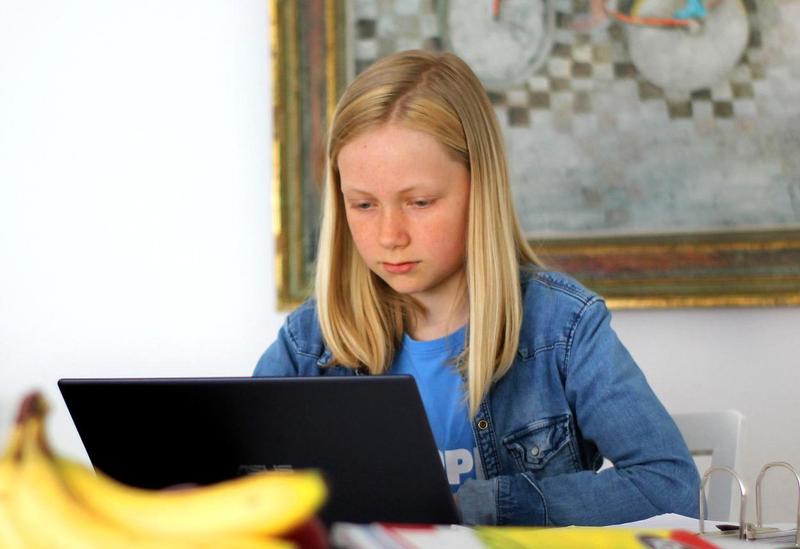Young girls reads from her laptop at the kitchen counter.