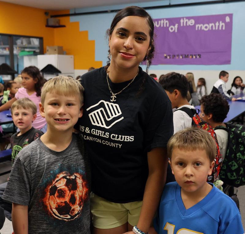A female staffer is flanked by two young boys and other children watch them from behind.