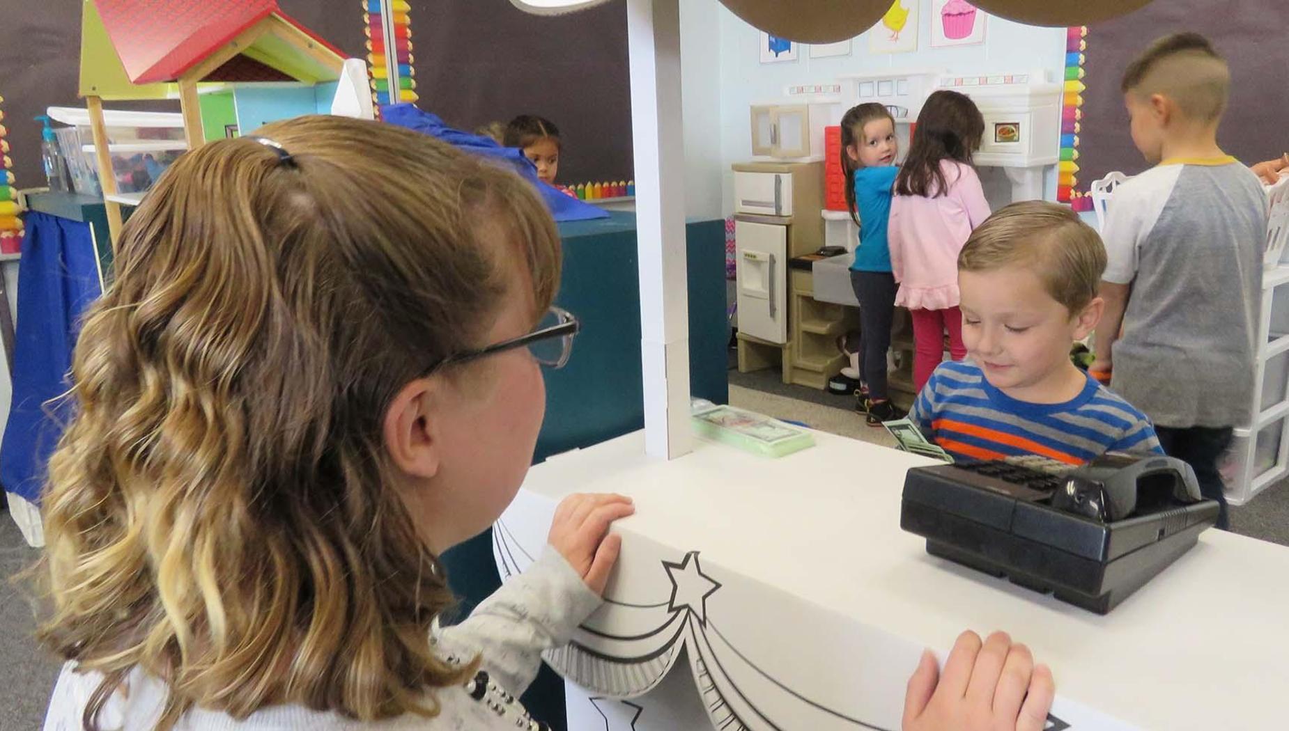 A young boy and his teacher play store.