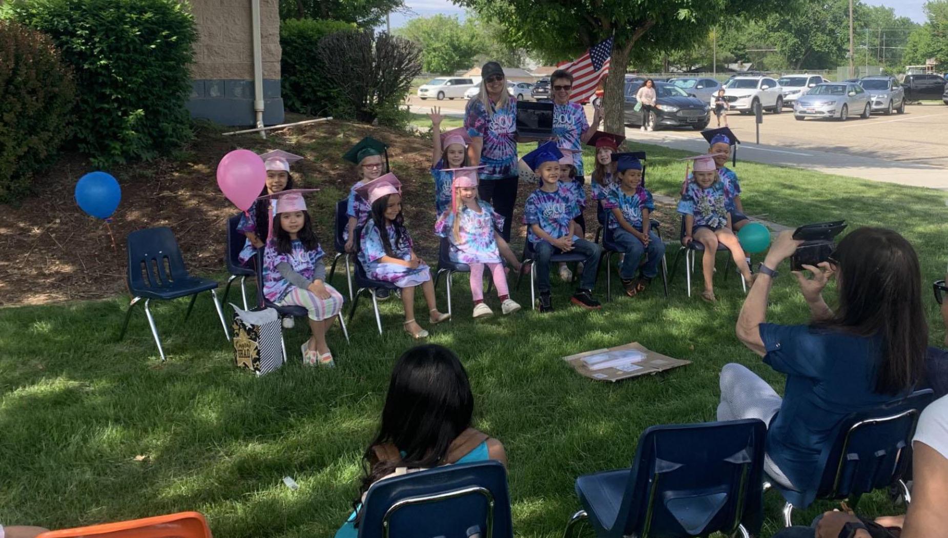Kindergartners sit and wait for graduation ceremony to start, wearing grad caps with tassels.