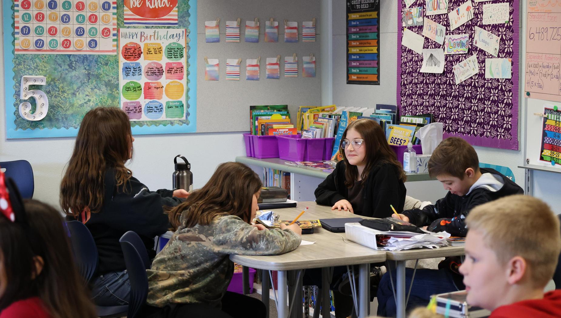 Four student work on worksheets while sitting at a long table.