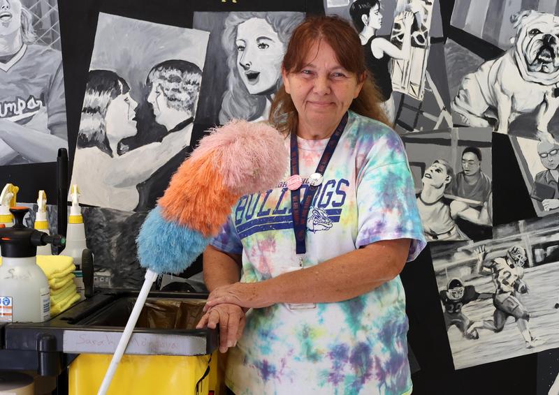 NHS Custodian Sarah Montoya stands with her cleaning cart in front of a mural at the school.