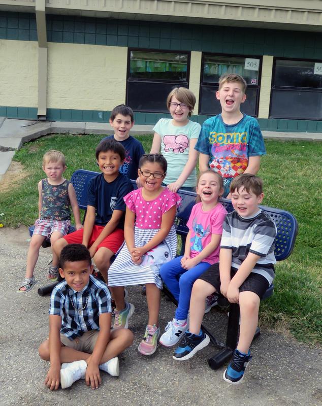 Elementary school children gather around a Buddy Bench and laugh.