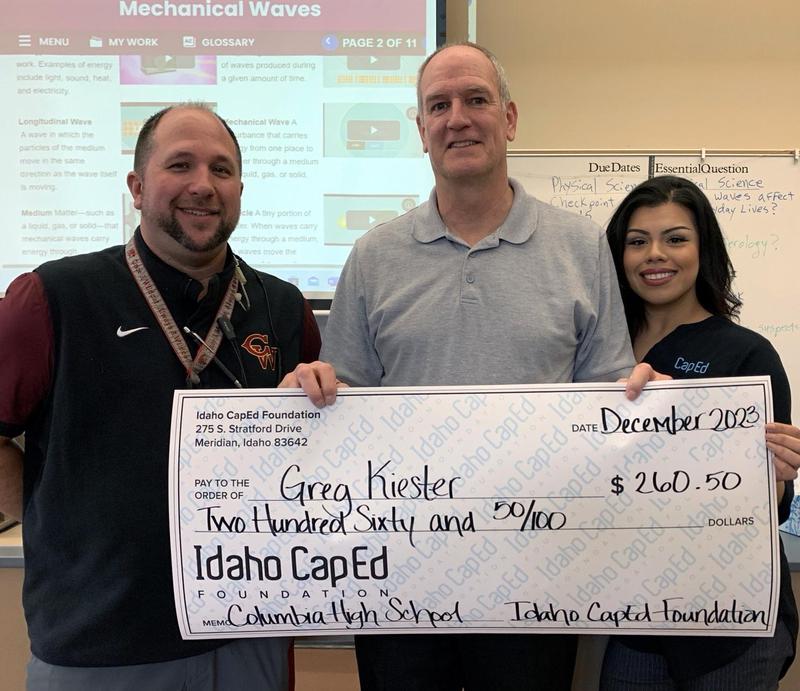 Nick Stern and AnaMaria Morales flank teacher Greg Kiester, holding an oversized donation check for $260.50.