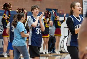 A male special education player claps, with girls cheerleading behind him.