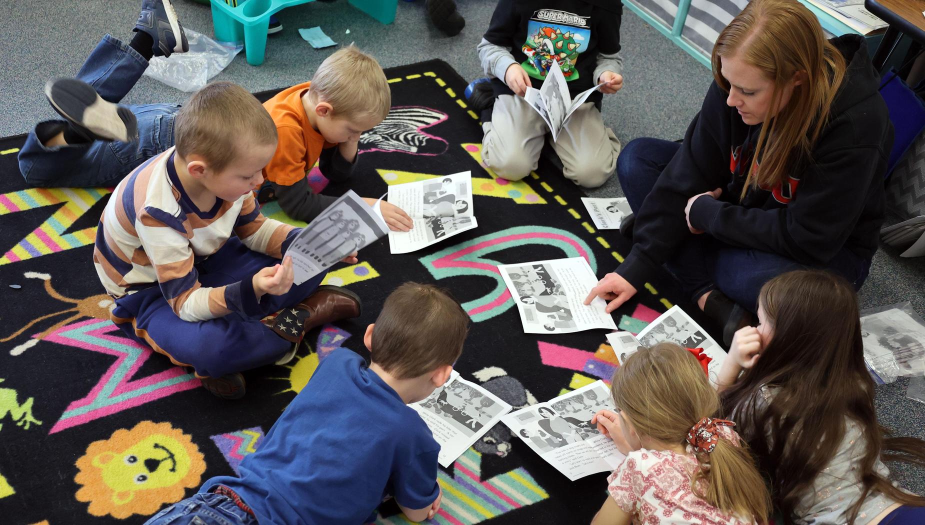 Teacher sits on rug with a circle of students working on a worksheet.