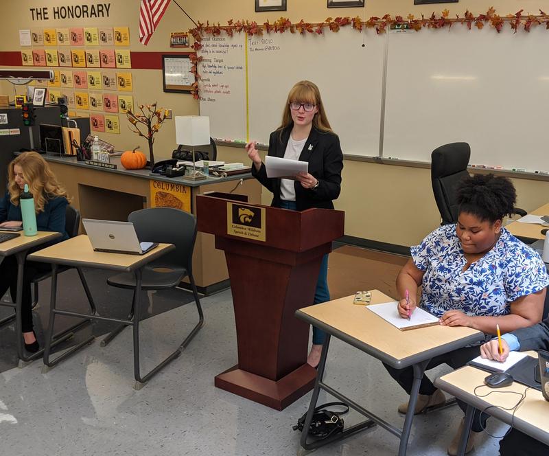 Debater competes at the podium while judges make notes.