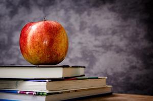 Red apple on a stack of three books in front of dark gray background.