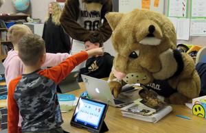 Montana State\'s mascot works on a computer while kids point at him in the classroom.