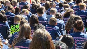 Students sit on the grass in matching school T-shirts during the ribbon-cutting ceremony.