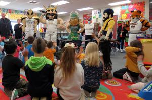 Four college mascots talk to kids seated on a classroom rug.