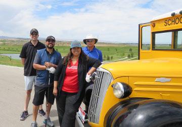 A team poses for a group shot with an antique school bus at RedHawk golf course.