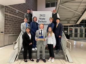 Debate team members pose on a staircase in front of the debate championship banner.