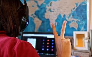 Back view of adult holding up two fingers in front of a computer monitor, with world map on wall in background.