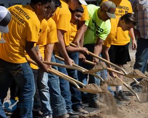 Students lift shovels of dirt at the groundbreaking.