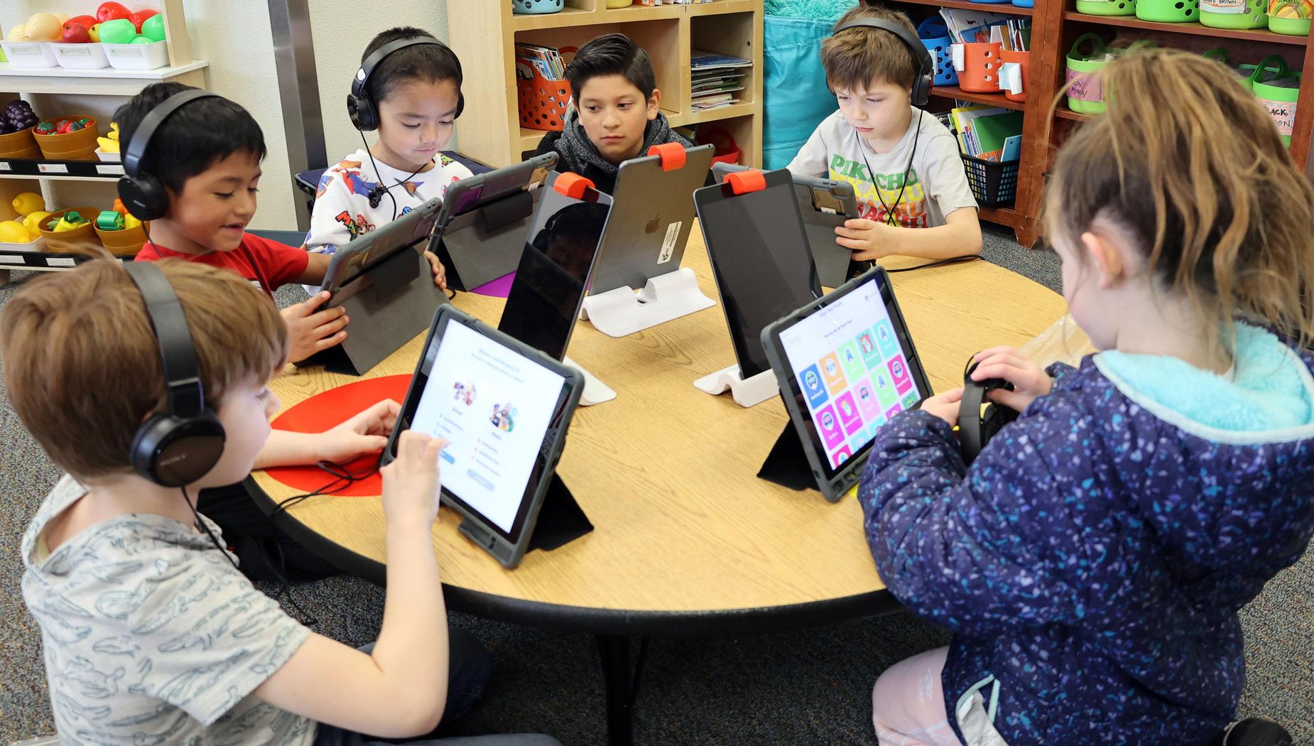 Children work on their iPads as they sit around a round table.