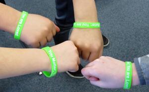 Four kids wearing green \"You Matter; You Are Loved\" bracelets bump fists.