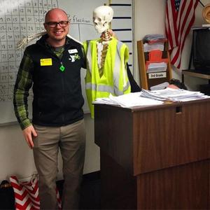 Alex Hackett poses in a classroom next to a skeleton wearing a safety vest.