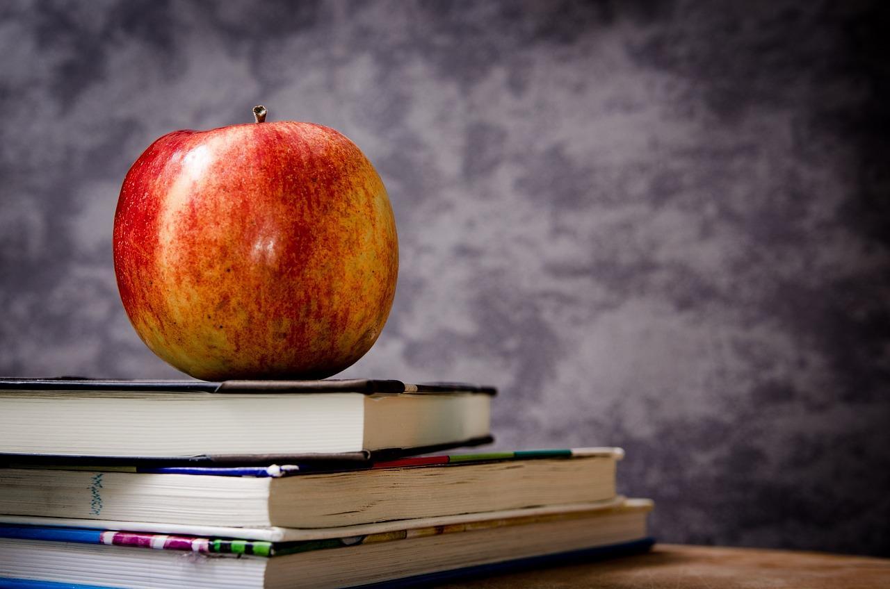 Red apple on a stack of three books in front of dark gray background.
