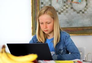 Young girls reads from her laptop at the kitchen counter.