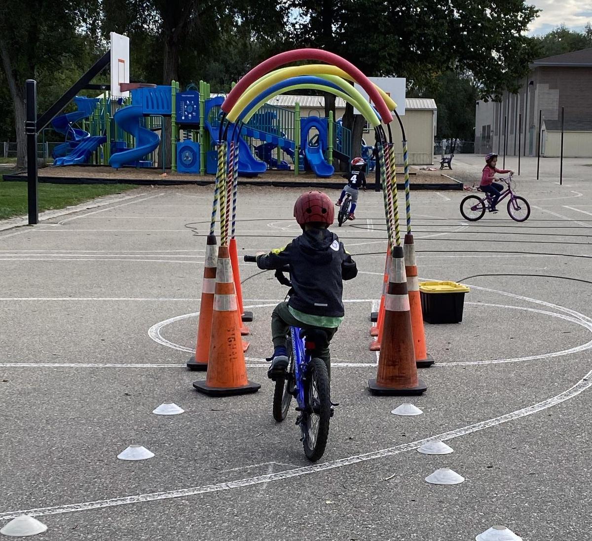 Child rides bike through hoops at a bike rodeo on a school playground.
