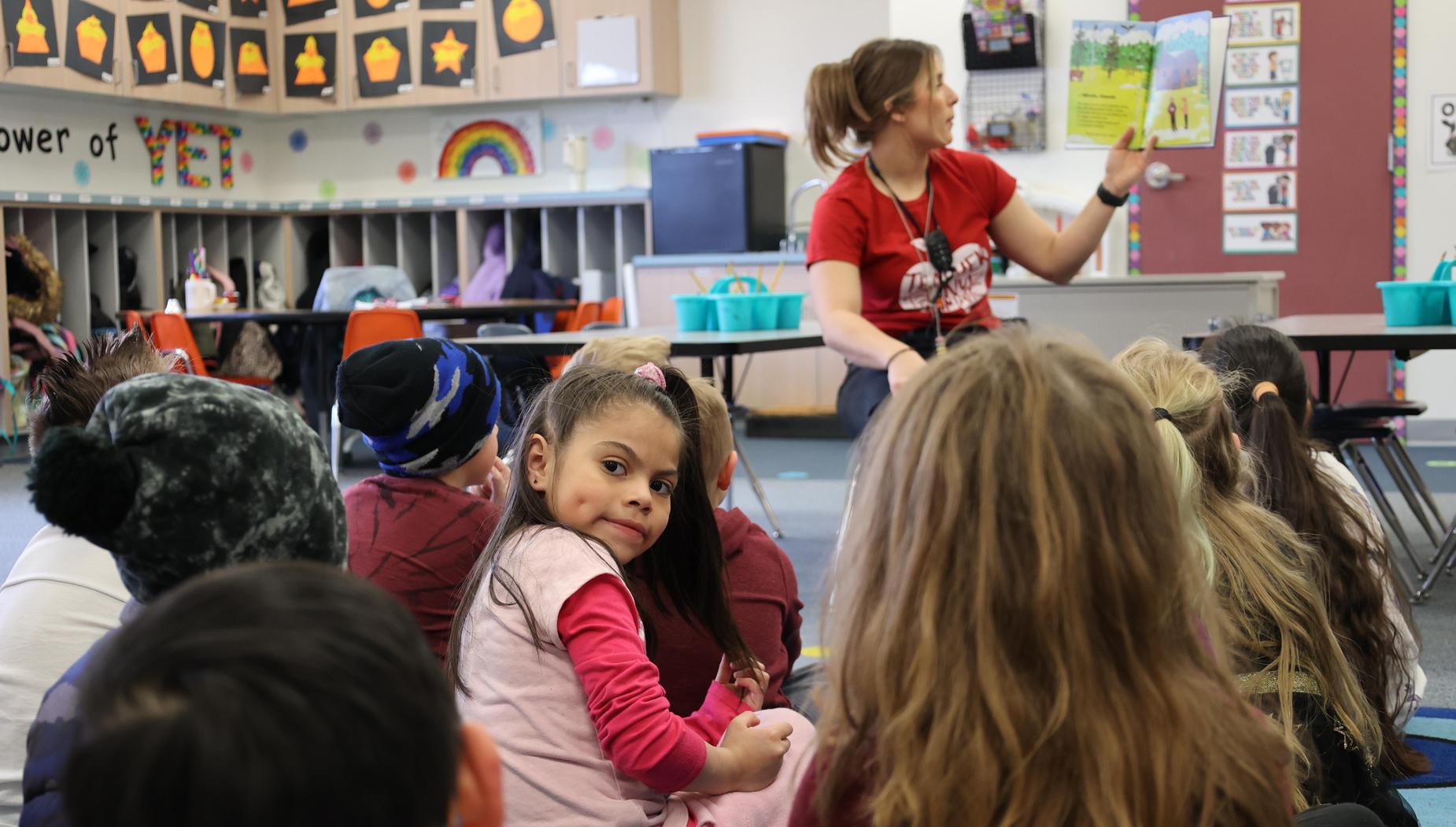 Teacher reads to students while one girl looks toward back of room.