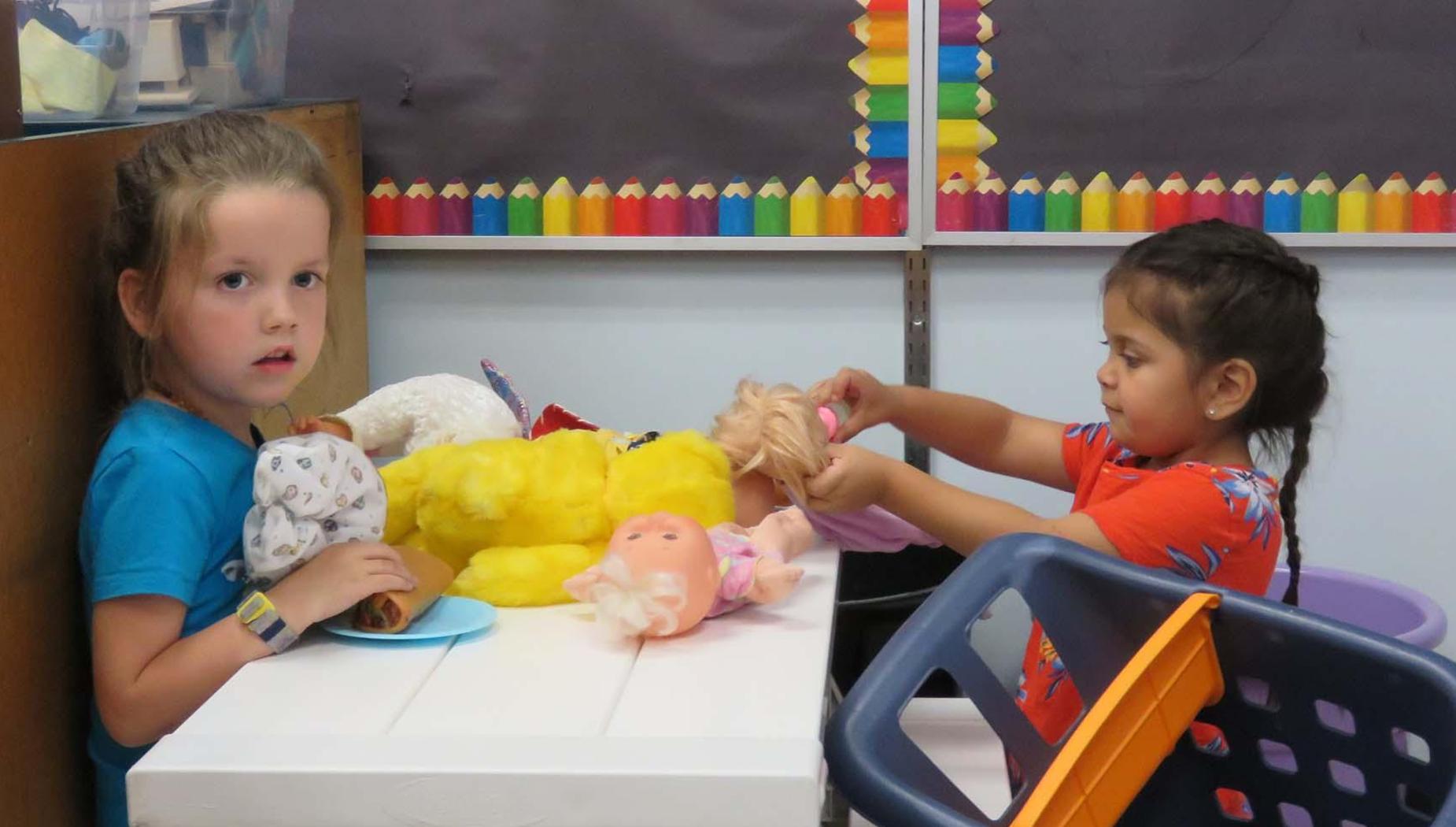 Two young girls play with stuffed animals and dolls.