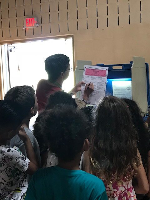 Woman holds up voting ballot for students to see.