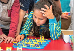 Girl with elbow on table and hand on head puzzling through the game of Guess Who.