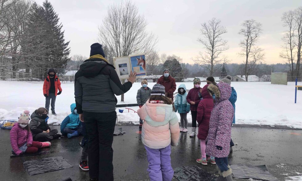 kids in a semi-circle looking a book about foxes held up by the teacher