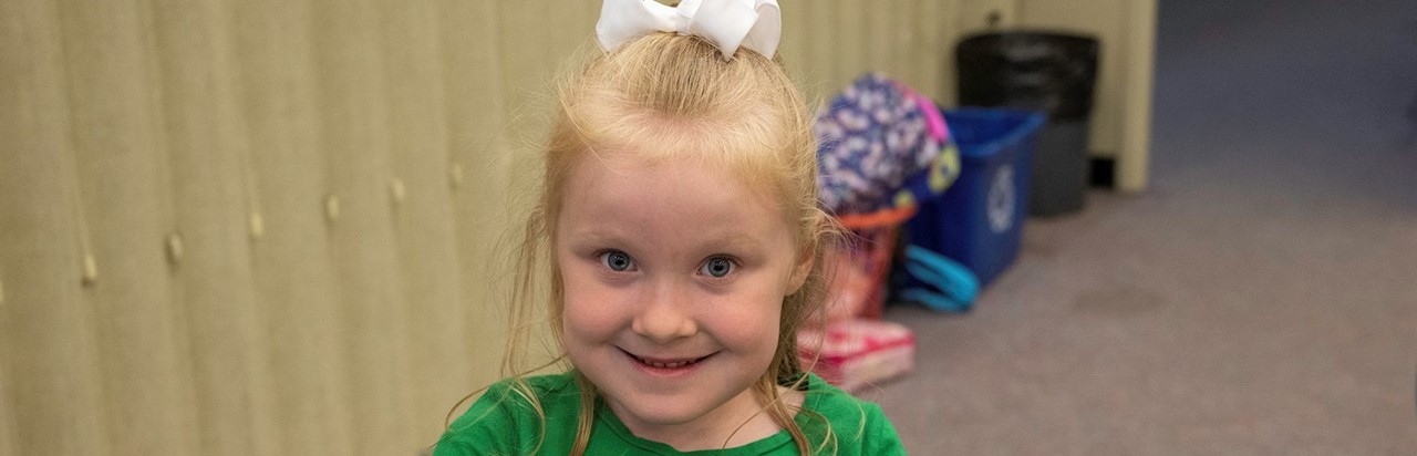 little blond girl with a green shirt and white hair ribbon