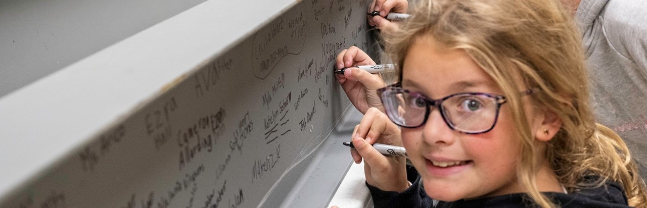 little blonde girl signing her name on a structural beam